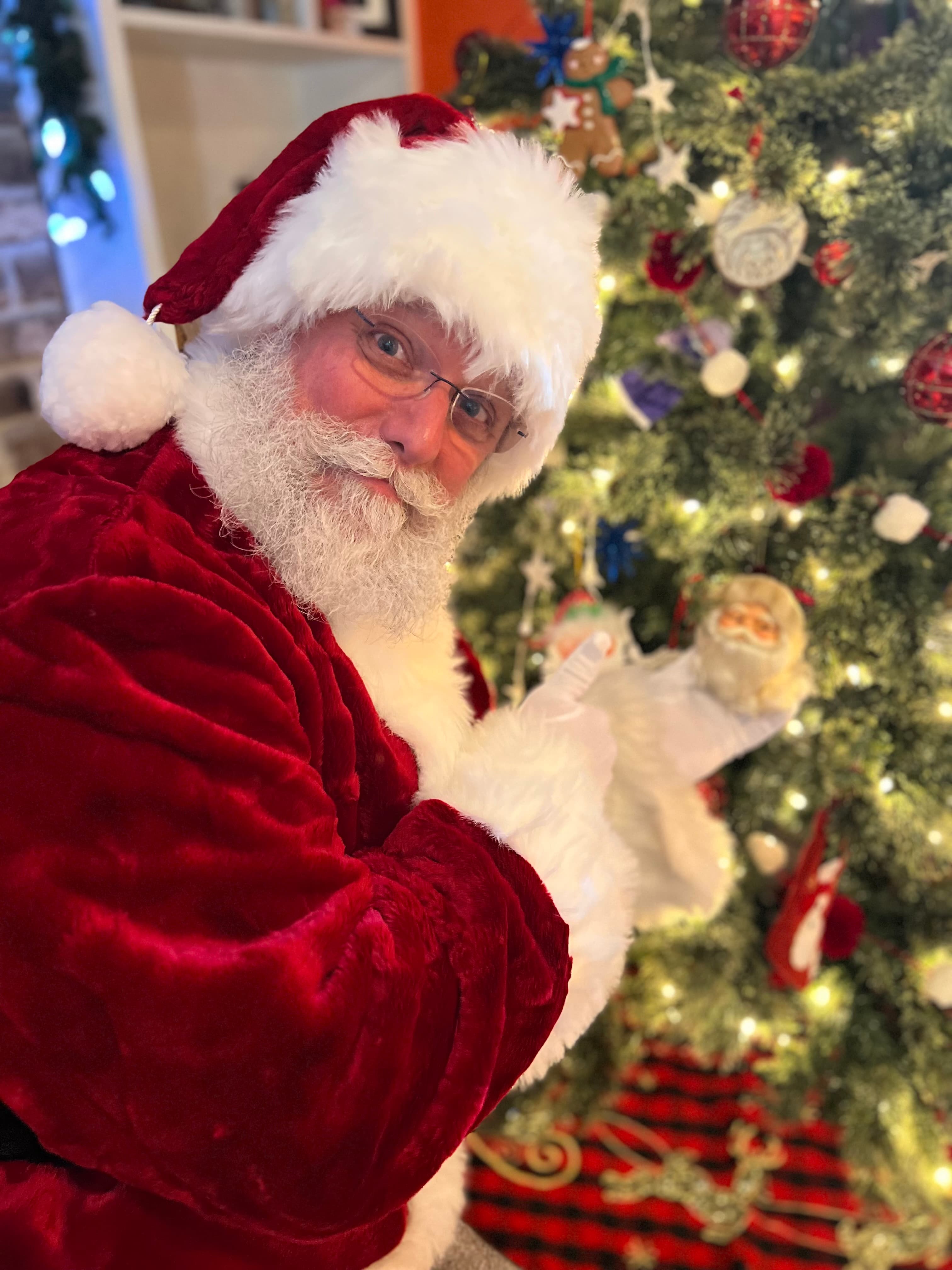 Santa Claus poses playfully beside a beautifully decorated Christmas tree.