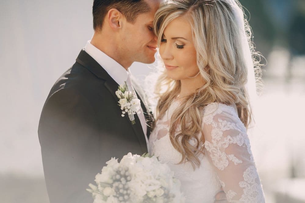 A couple embraces softly, with the bride holding a bouquet and both looking serene.