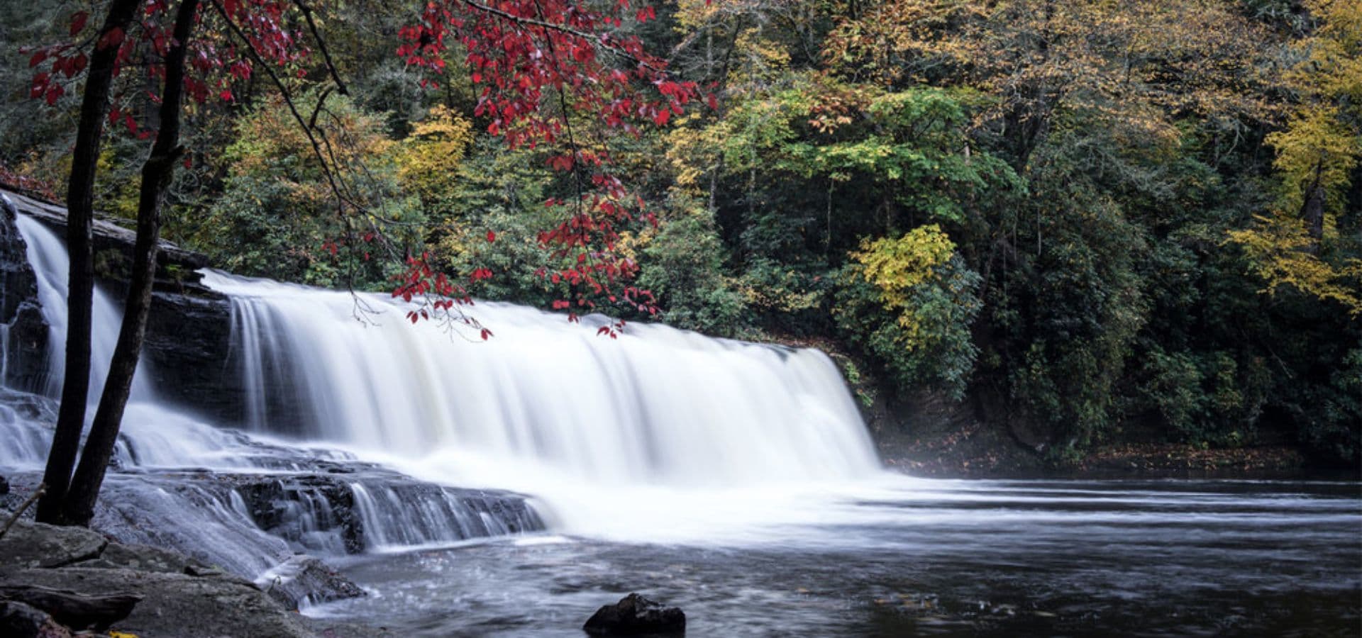 A serene waterfall surrounded by colorful autumn foliage.