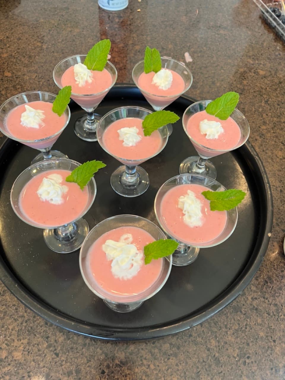 A tray with eight dessert cups filled with pink mousse, each topped with whipped cream and mint leaves.