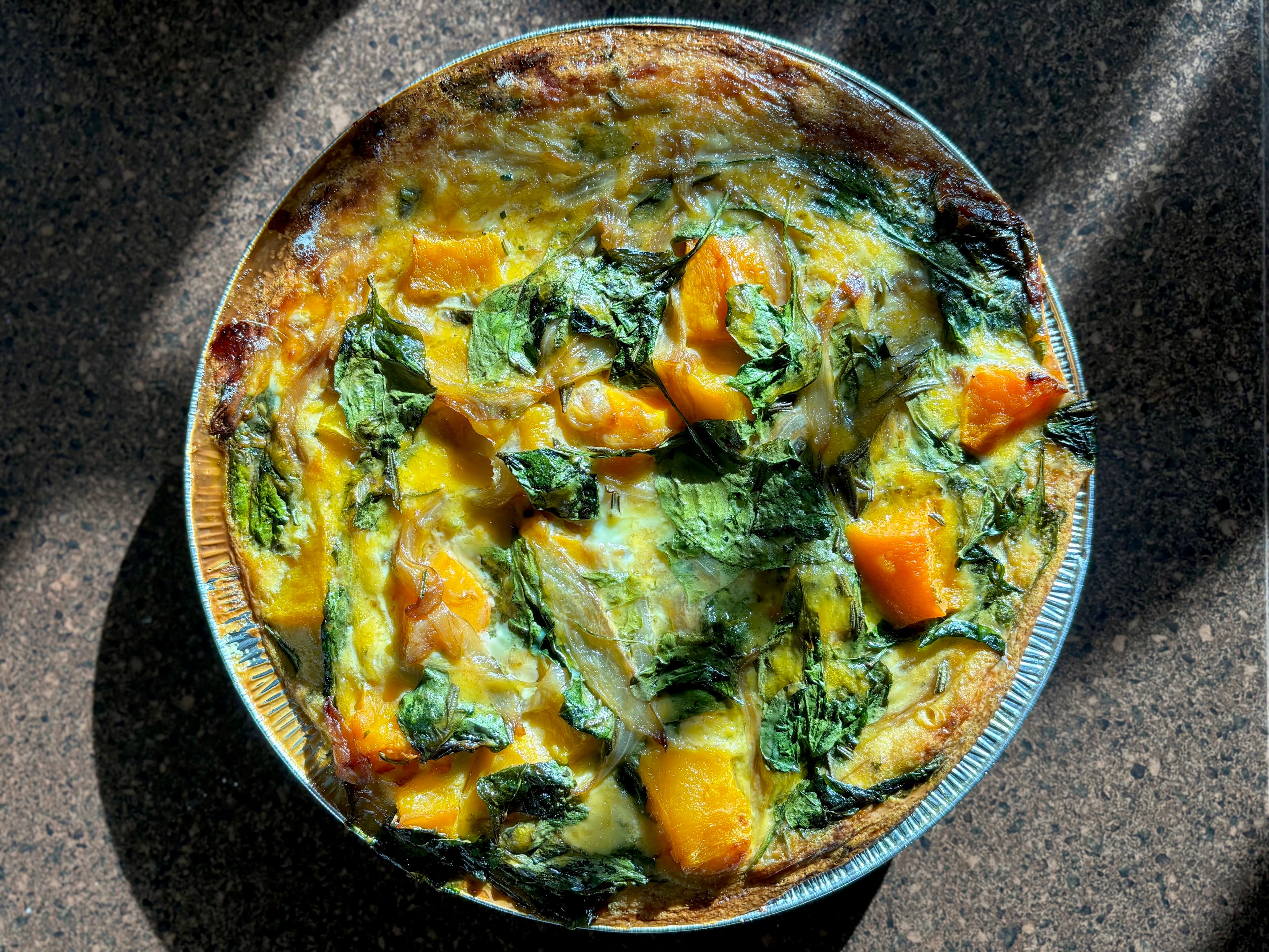 A baked frittata with pumpkin and leafy greens in a round tin.
