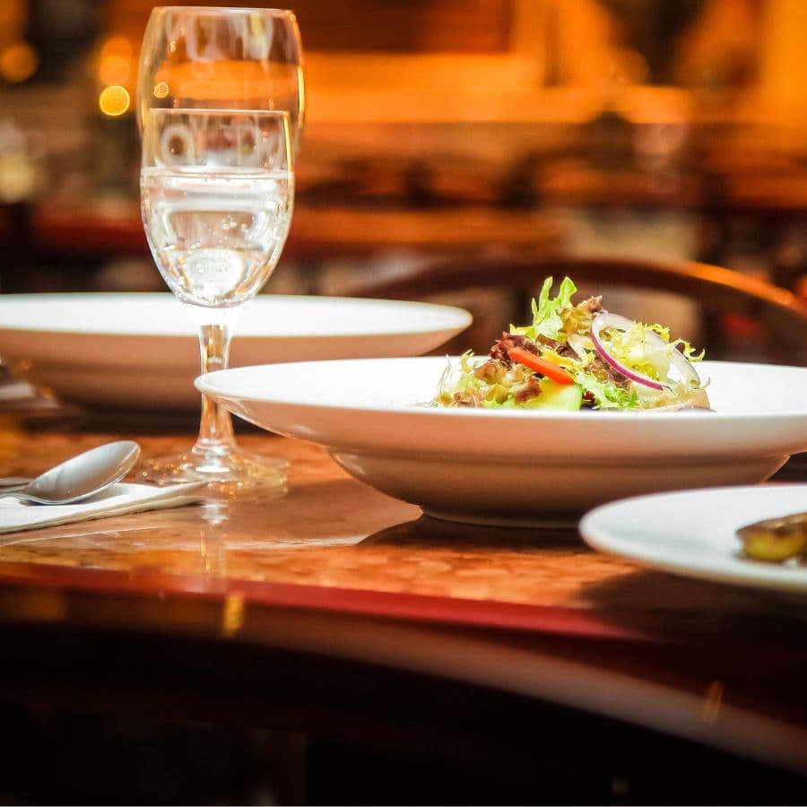 A plate of salad sits on a table set with a glass of water and silverware.