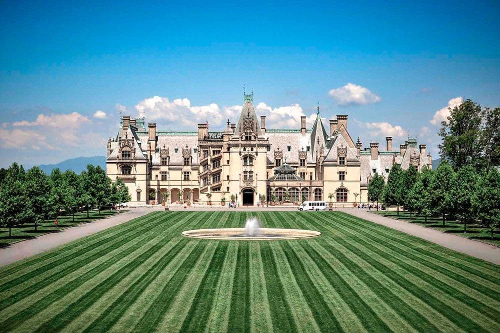A grand mansion surrounded by neatly trimmed lawns and trees under a clear blue sky.