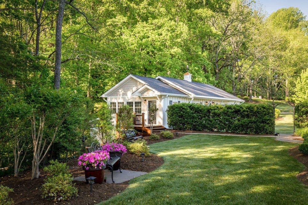 A charming white cottage surrounded by lush greenery and colorful flowers.