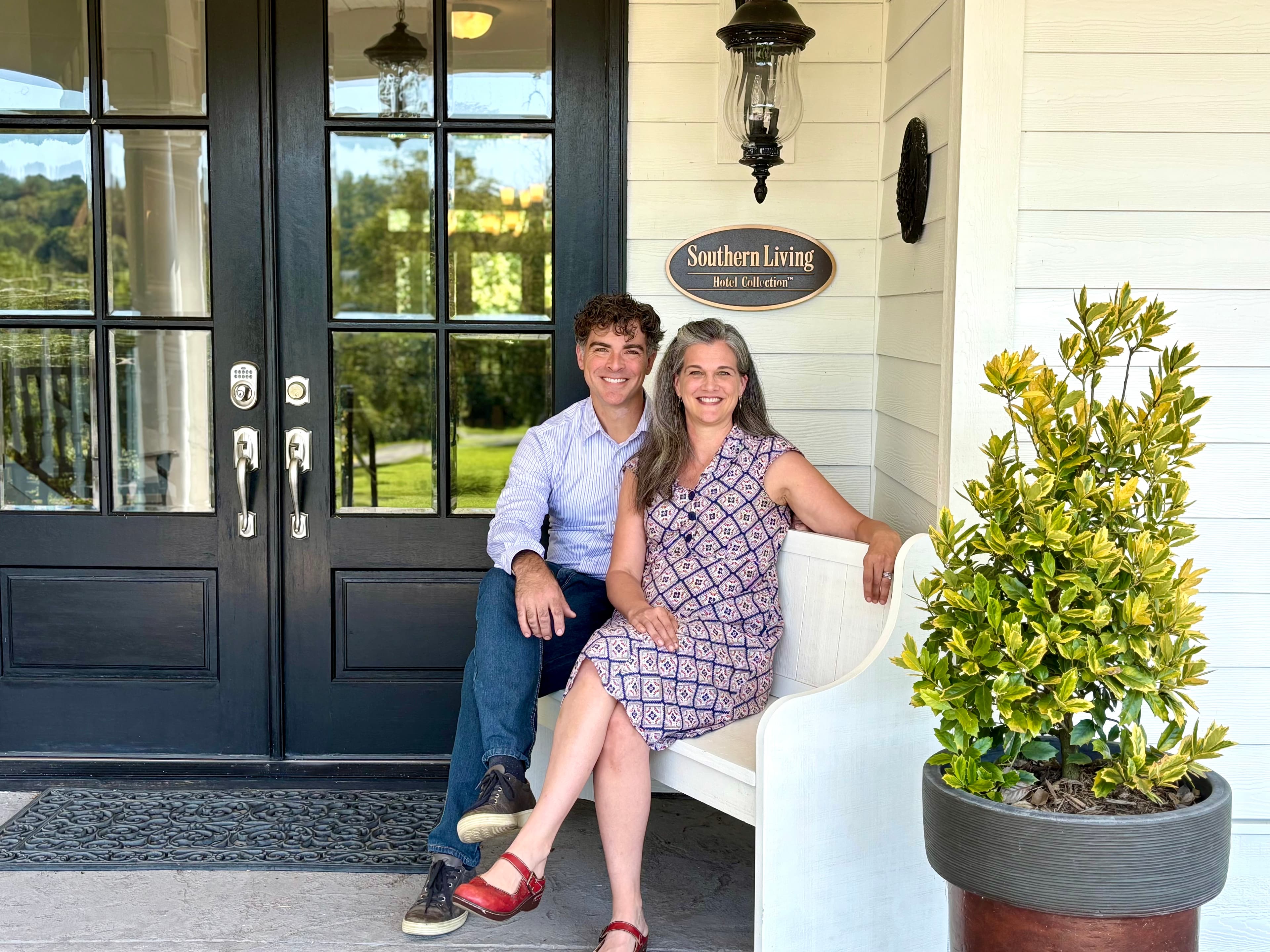 A man and woman are sitting together on a bench outside a house with a sign labeled "Southern Living."