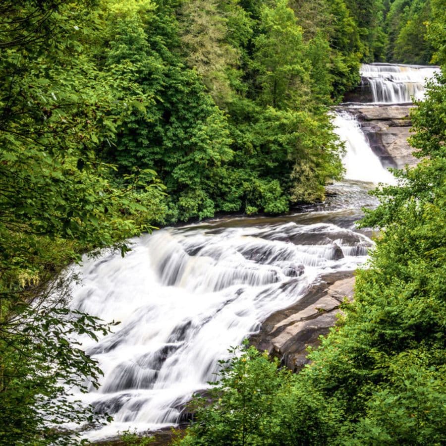 A picturesque waterfall cascading down rocky steps, surrounded by lush green trees.