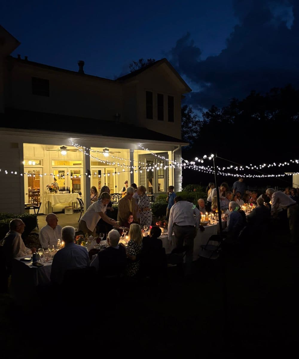 A group of people dining outdoors under string lights during a night gathering.