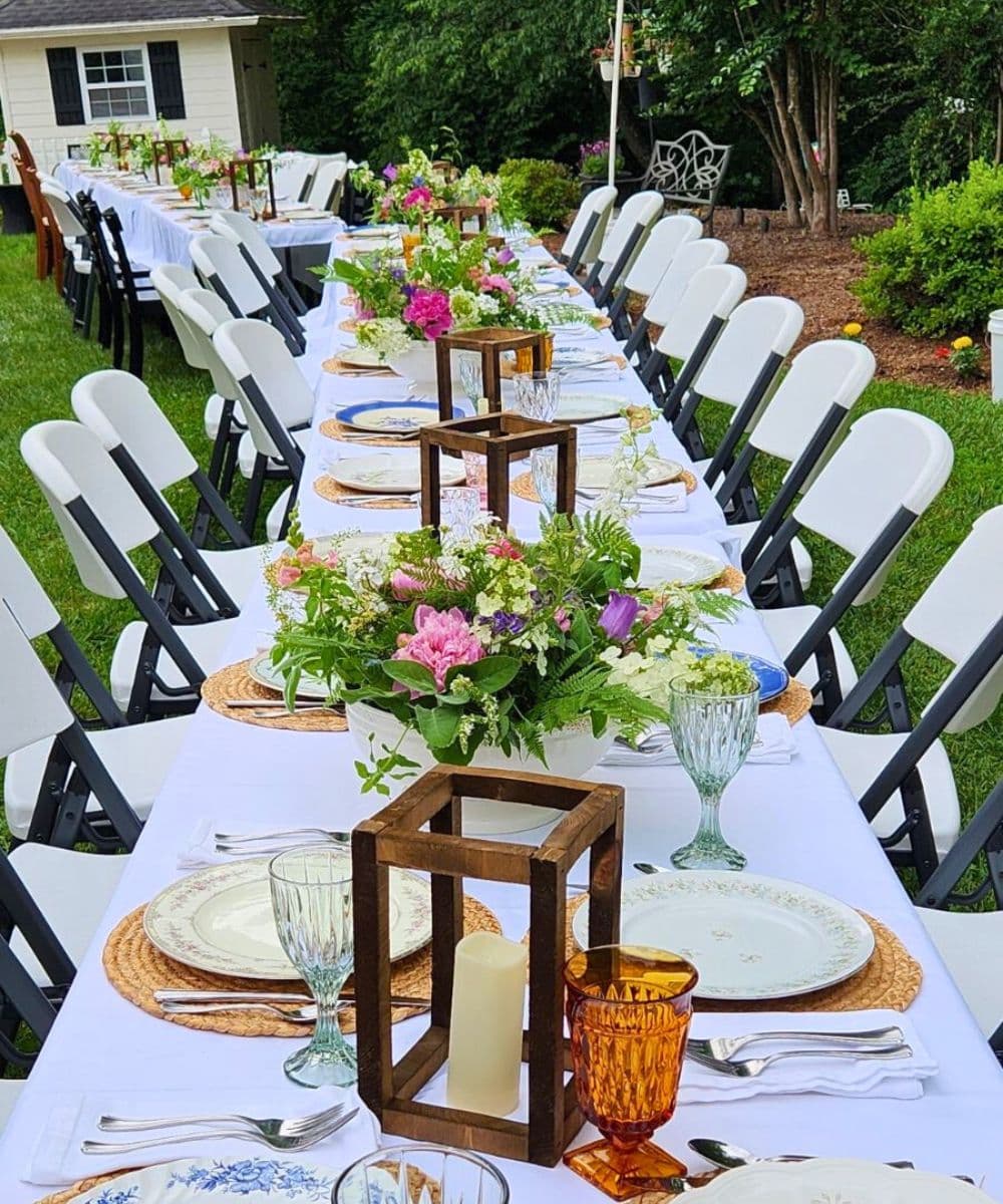A beautifully set outdoor dining table adorned with floral centerpieces, elegant tableware, and colorful glassware.