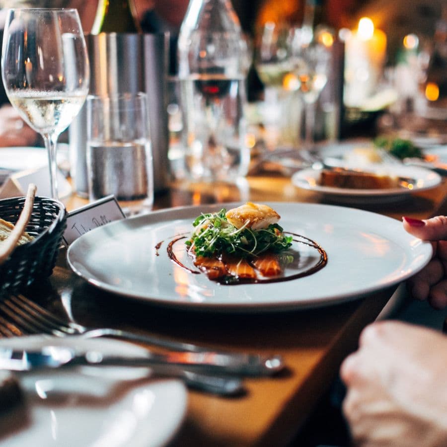 A beautifully plated dish garnished with greens, accompanied by wine glasses and a cozy dining atmosphere.