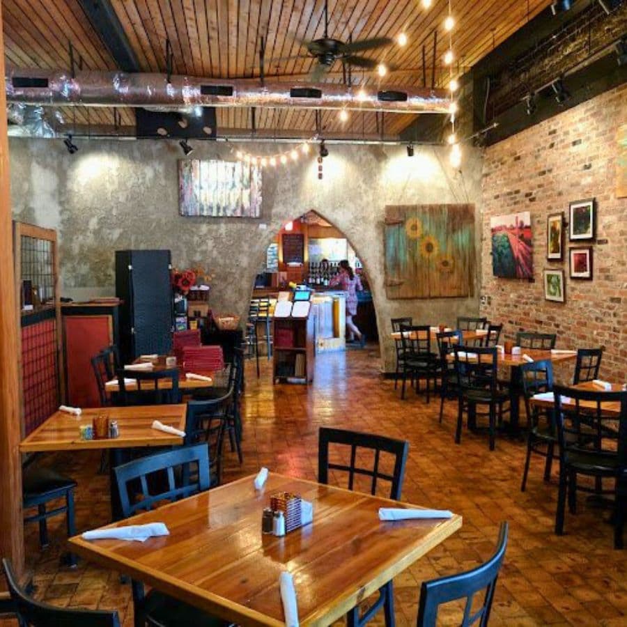 A cozy restaurant interior featuring wooden tables, black chairs, and artistic wall decor.