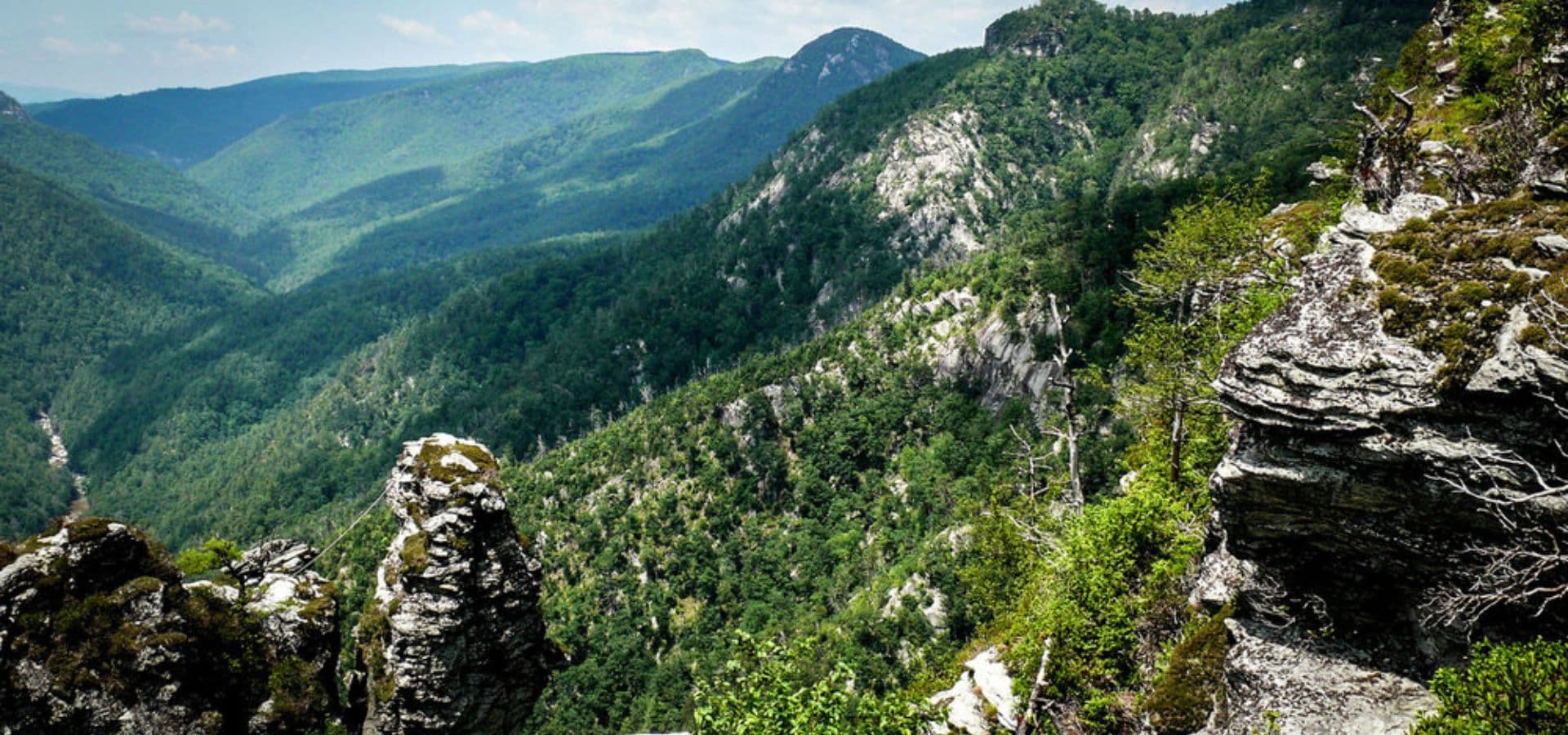 Lush green mountains and rocky cliffs under a clear blue sky.