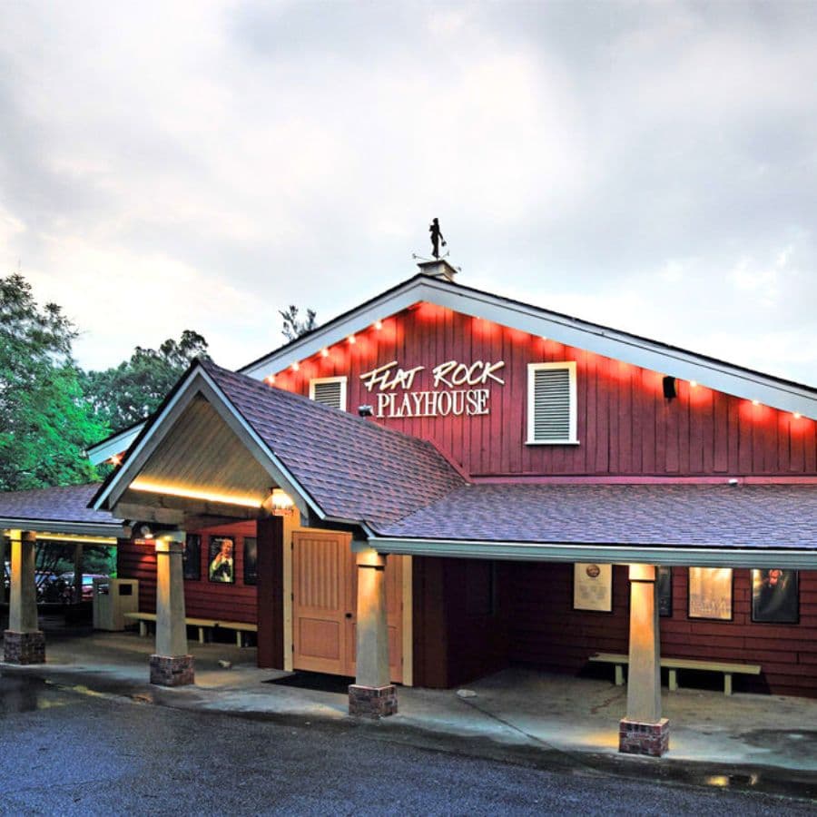 The exterior of the Flat Rock Playhouse, a red wooden building with a sloped roof and a sign above the entrance.