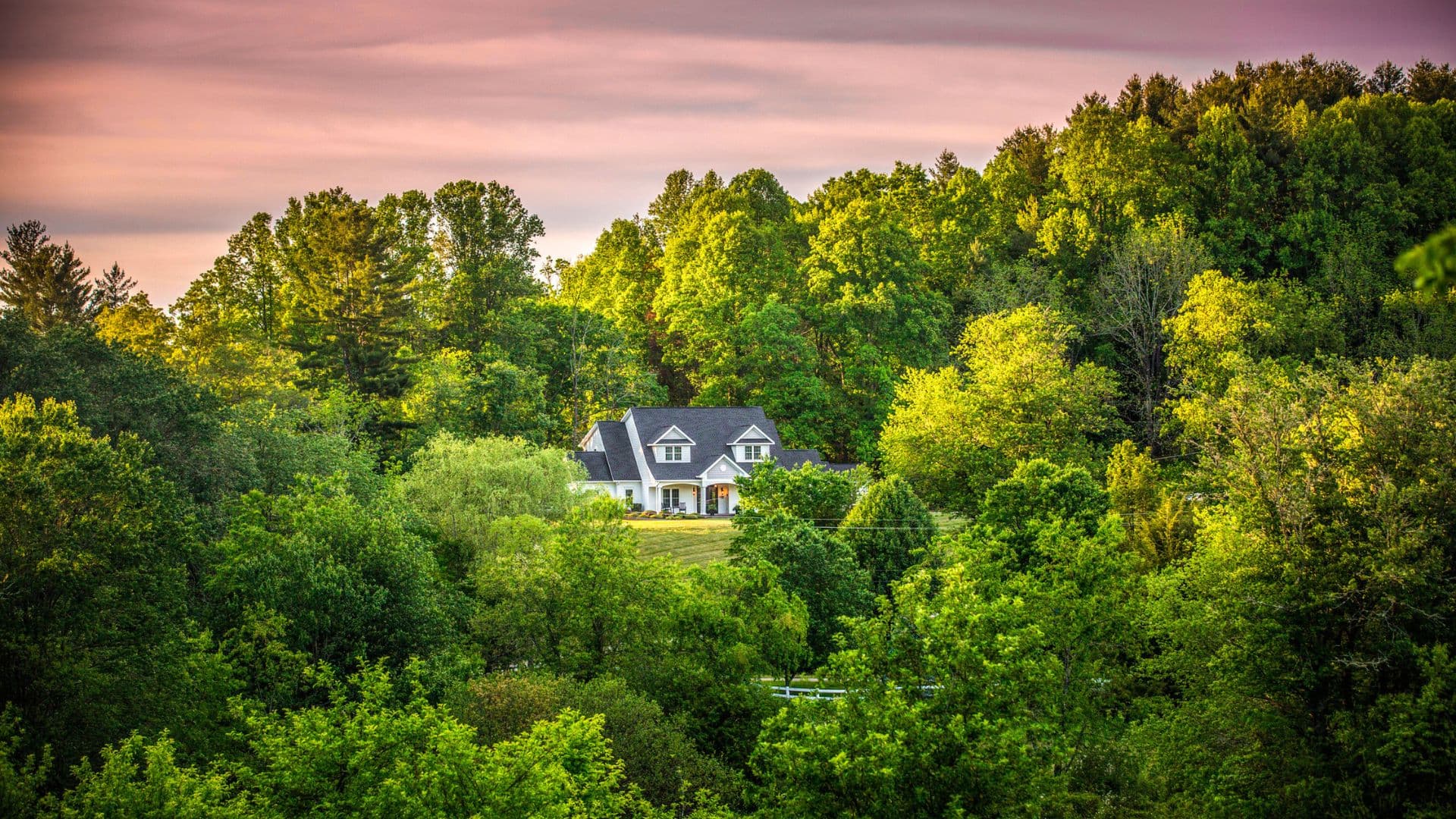 A large white house surrounded by lush green trees under a colorful sky.