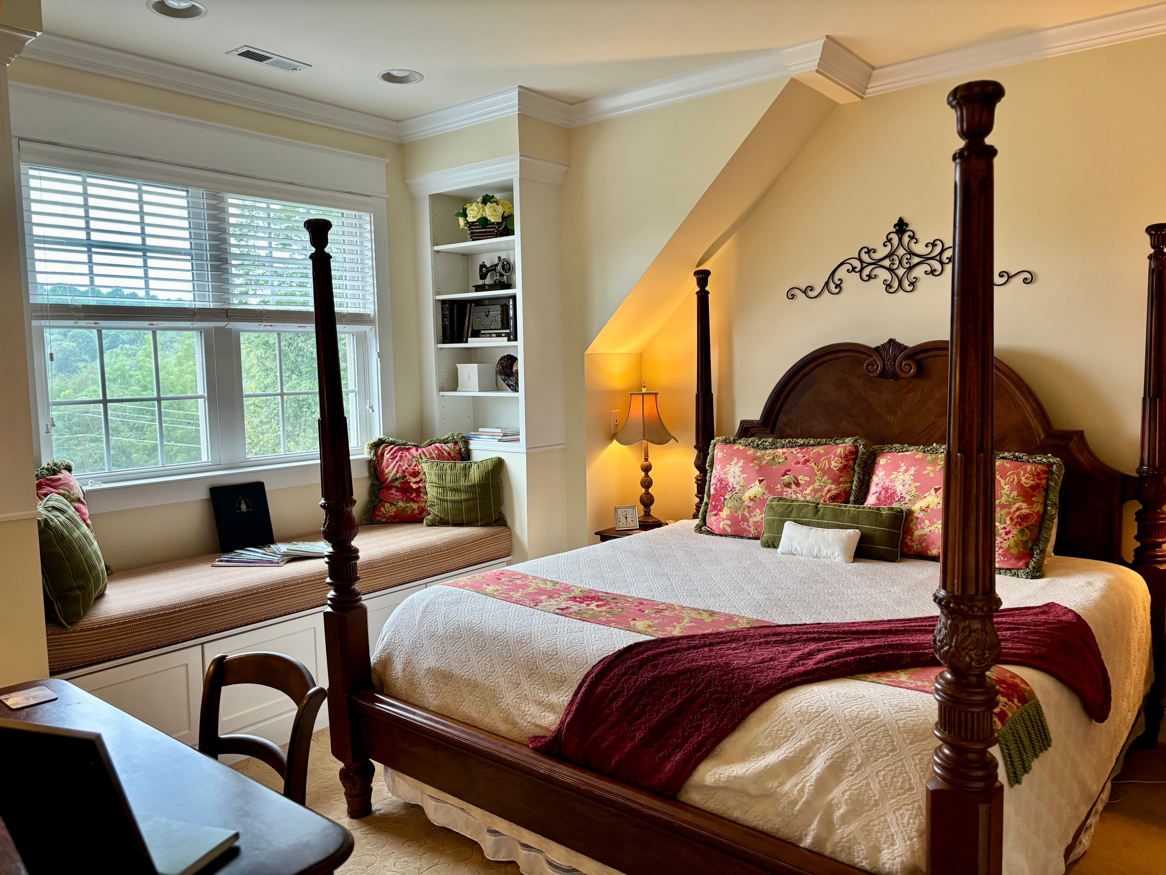 A cozy bedroom featuring a four-poster bed, a window nook with cushions, and decorative accents.
