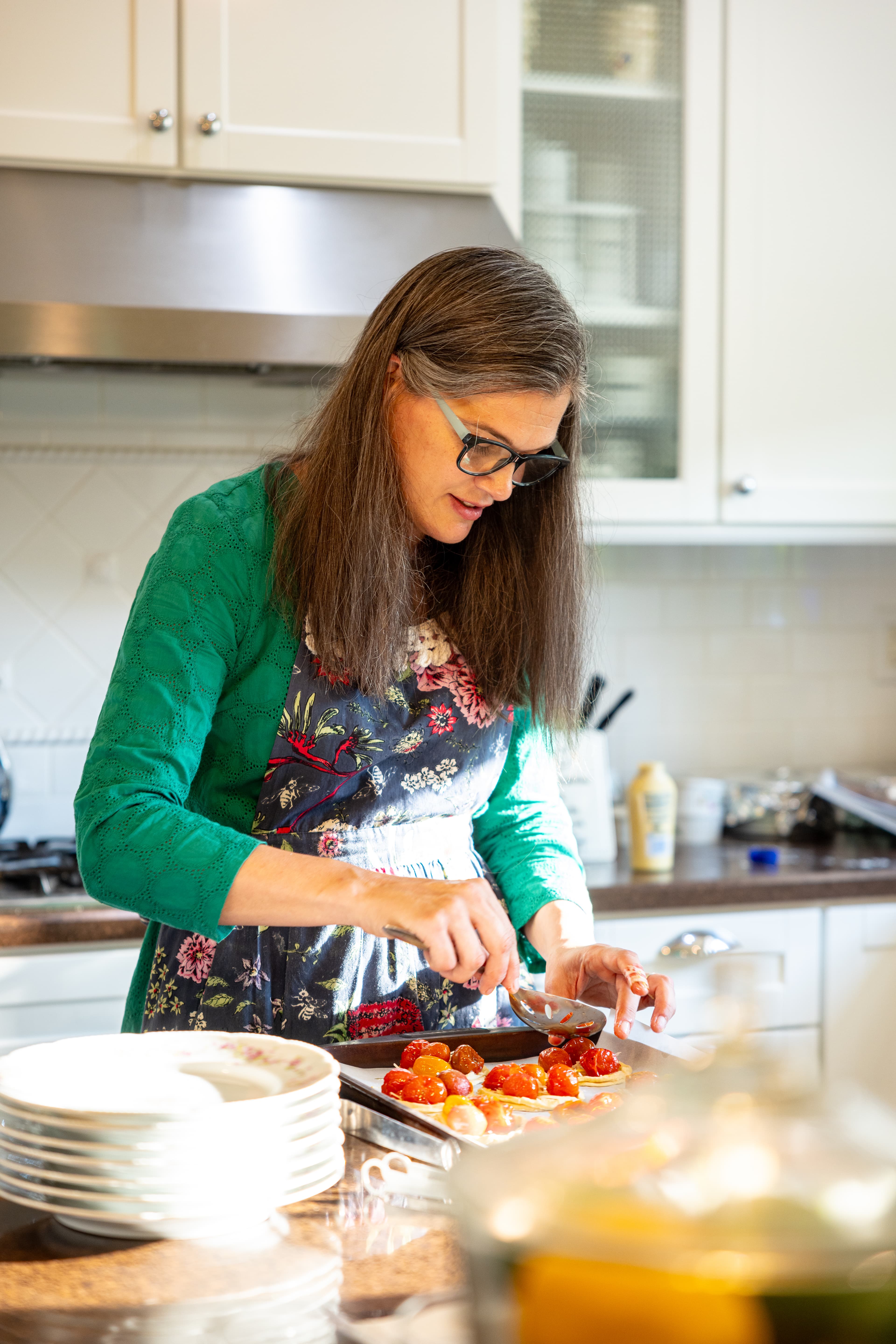 A woman in a green dress wearing an apron in her kitchen making fruit tarts
