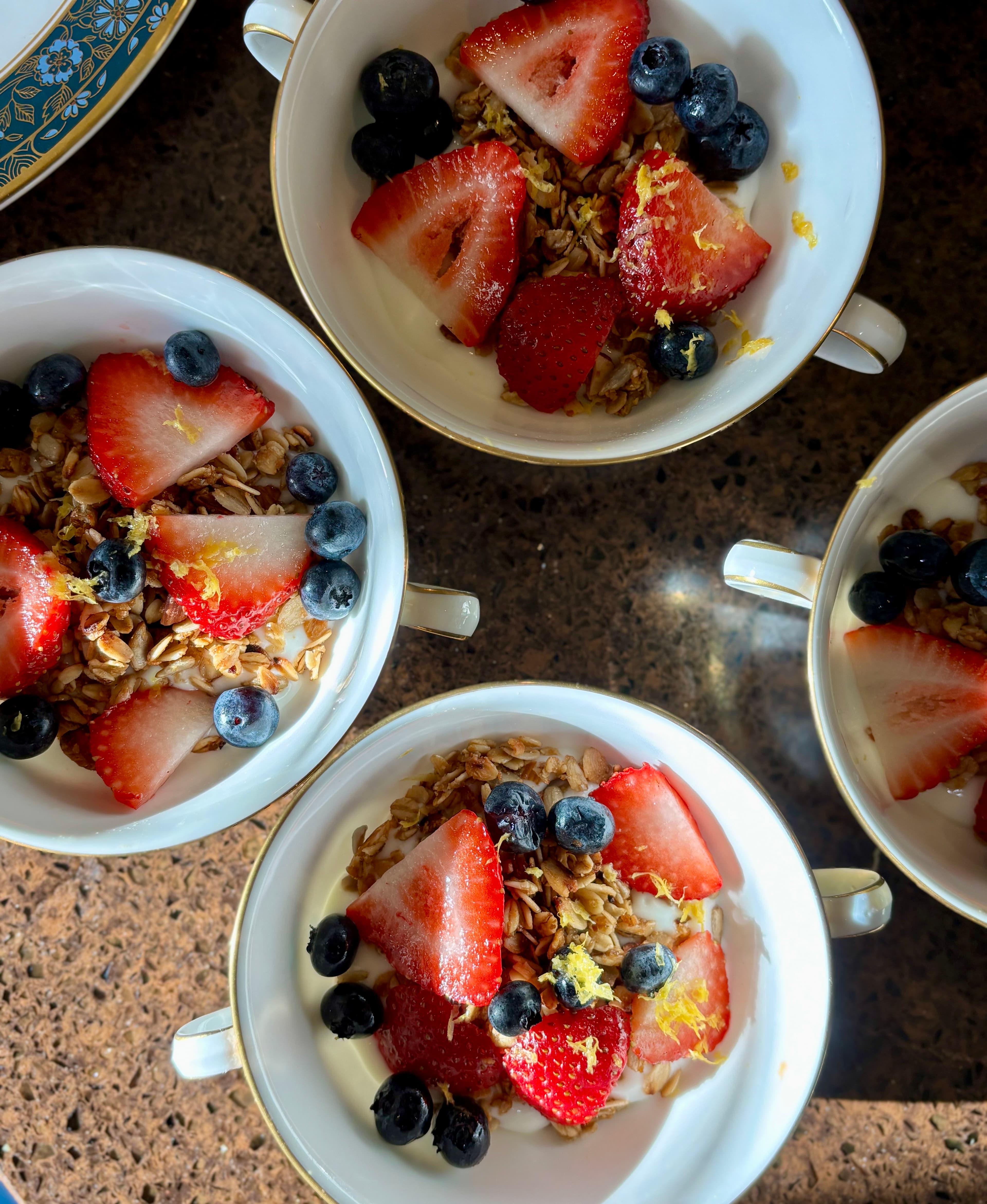 Aerial view of four white bowls filled with granola, strawberries, and blueberries.