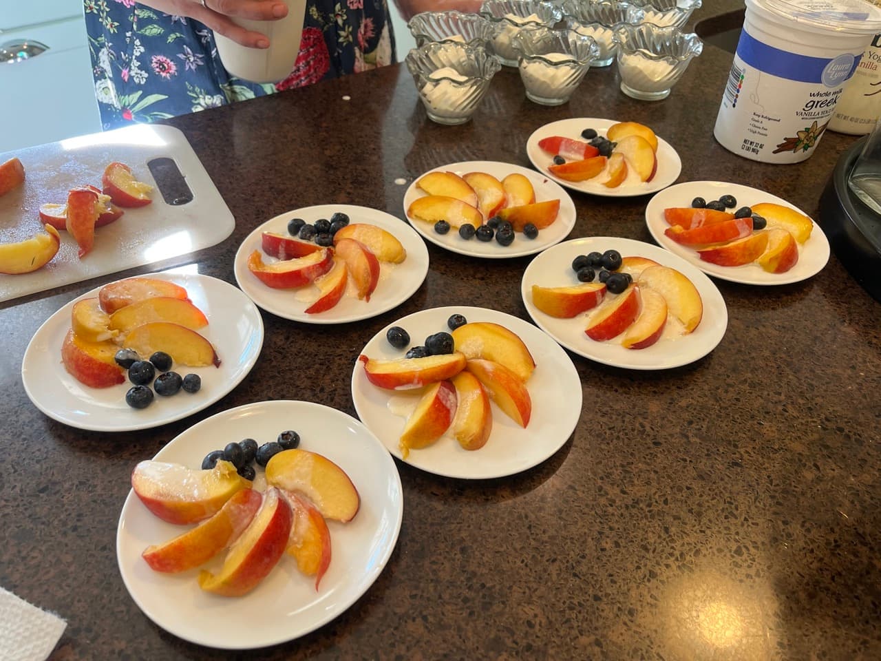 Sliced peaches and blueberries arranged on small plates with a bowl of yogurt in the background.